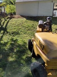 The wood chipper moves down the slope. Behind it, next to the building, lies a large pile of mulch left over from grinding the stump.