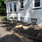A freshly cut tree stump next to a white brick house.